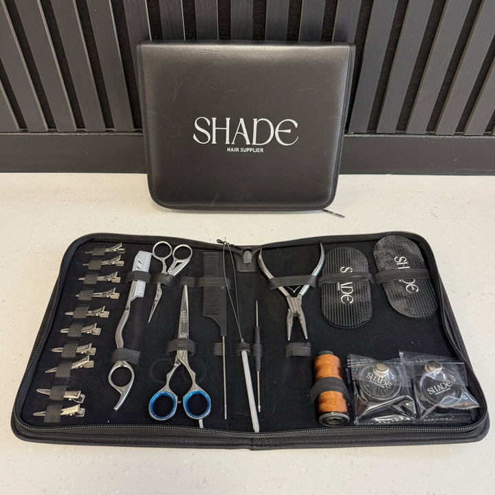 A hair extension application kit from Shade Hair Supply, shown open on a light countertop with its black carrying case standing behind it. The kit contains multiple tools including scissors, clips, pliers, and thread, with the brand name 'SHADE' clearly visible on the case.